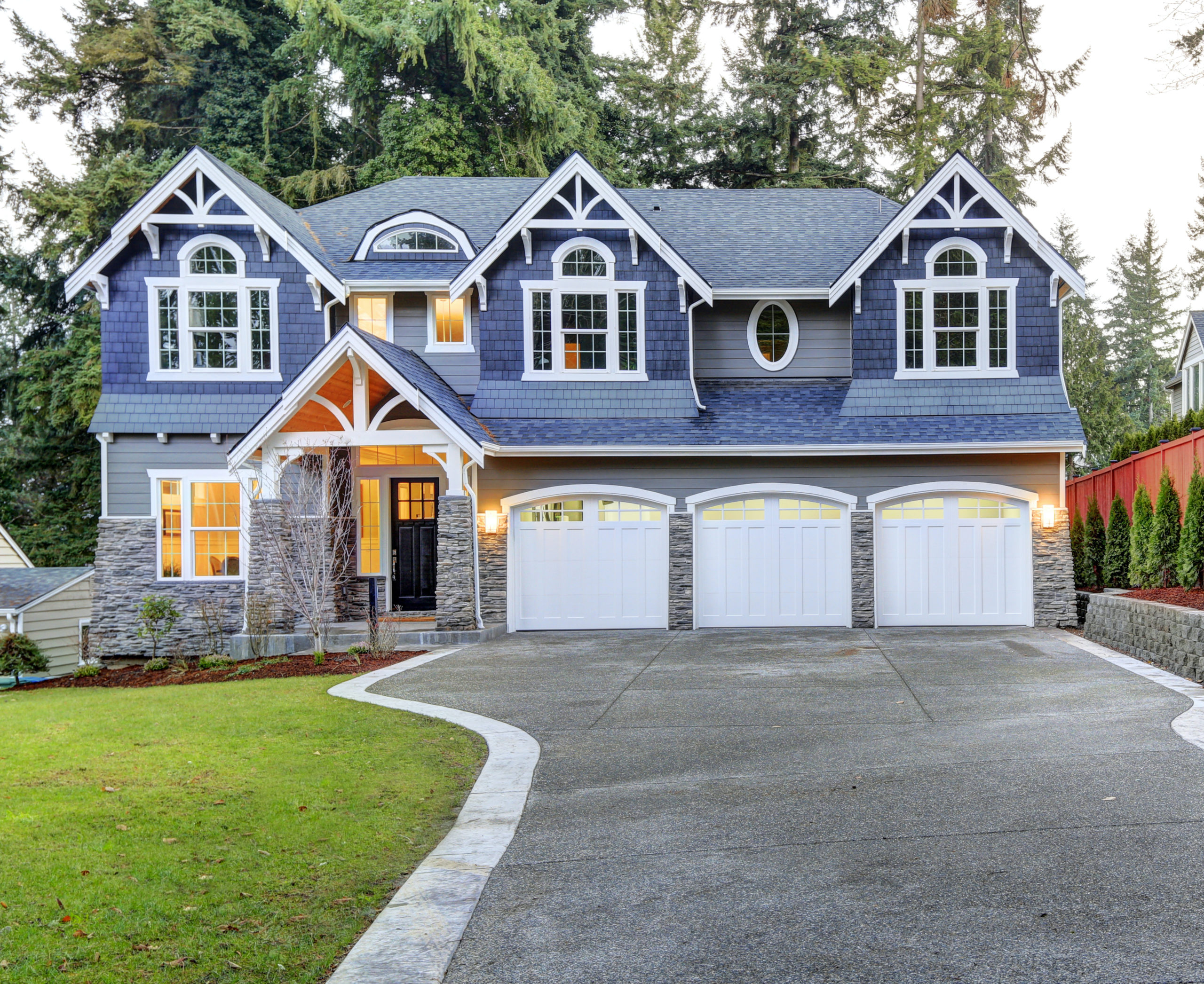 Luxurious home exterior with blue vinyl siding and white trim. Long concrete driveway lead to three attached garage spaces. Beautiful curb appeal.