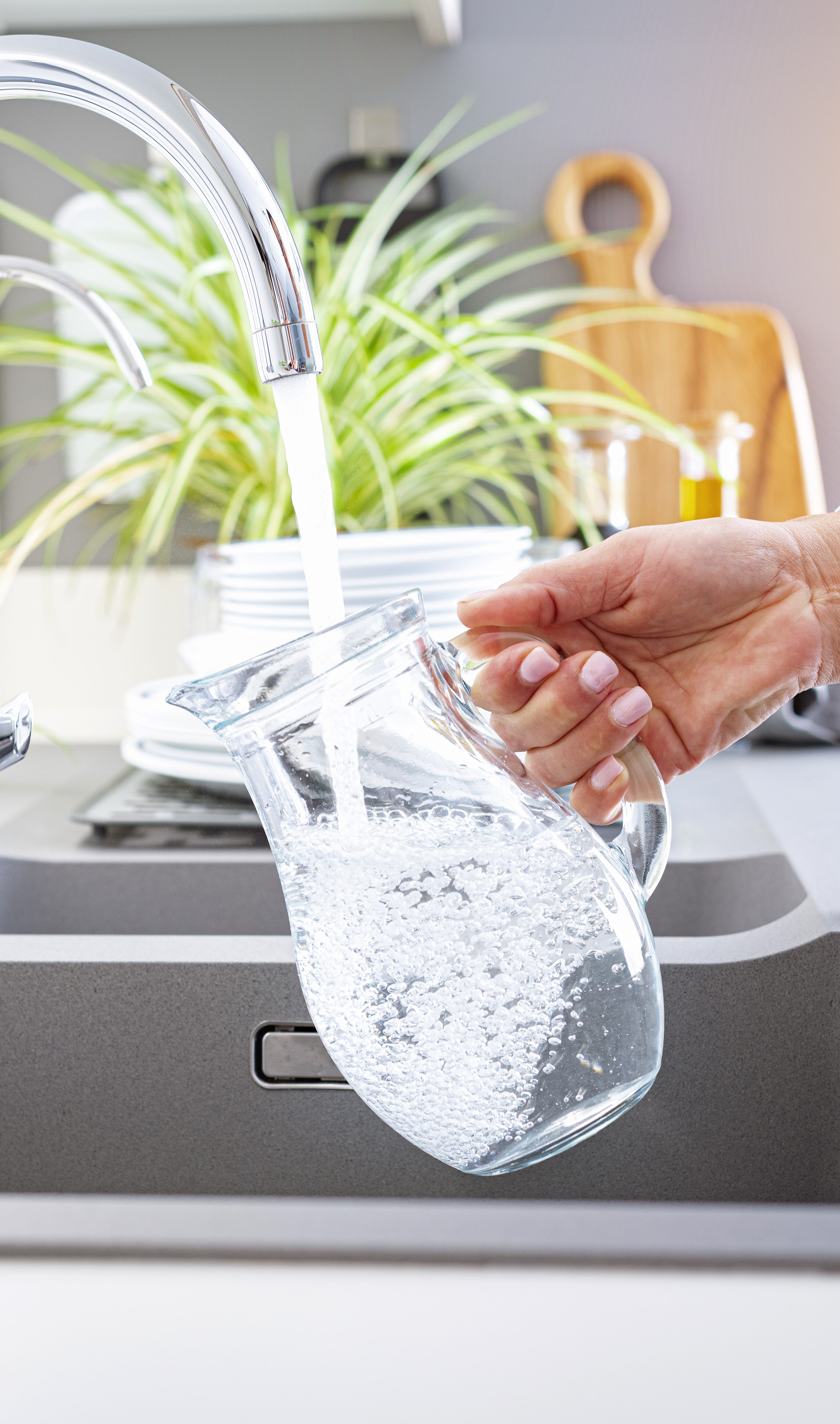Image of woman's hand with freshly manicured fingernails filling a clear pitcher with water from the kitchen faucet